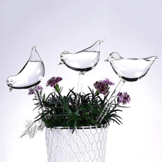 Pot blanc avec fleurs et verdures dans lequel sont piqués 3 tiges en forme d'oiseau remplis d'eau pour l'arrosage.
